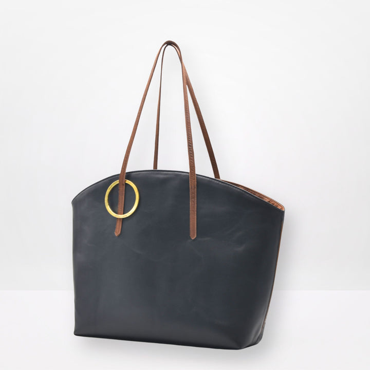 Black tote bag with brown handles and a gold ring on a white background