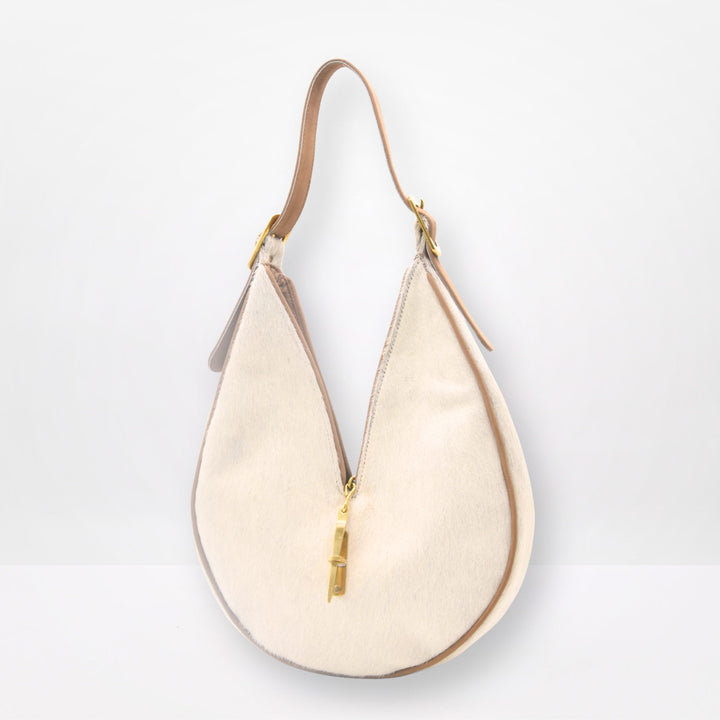 Round sculptural shoulder bag in cream cowhide with gold-brass hardware and signature closing system, handmade by Patricia Bos Designs.