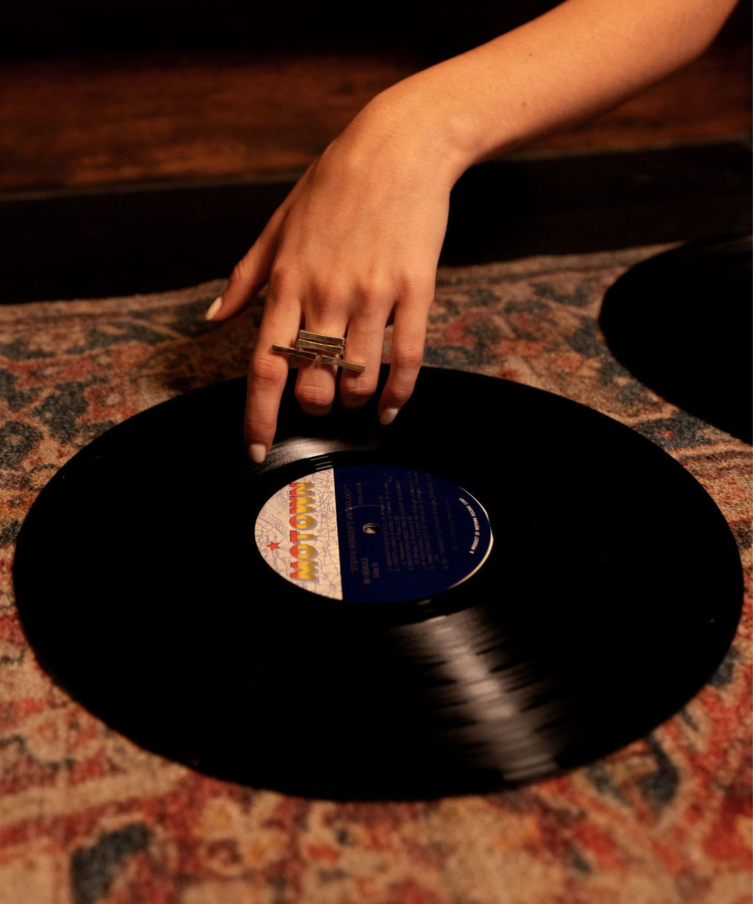 Hand with a ring holding a vinyl record on a patterned surface